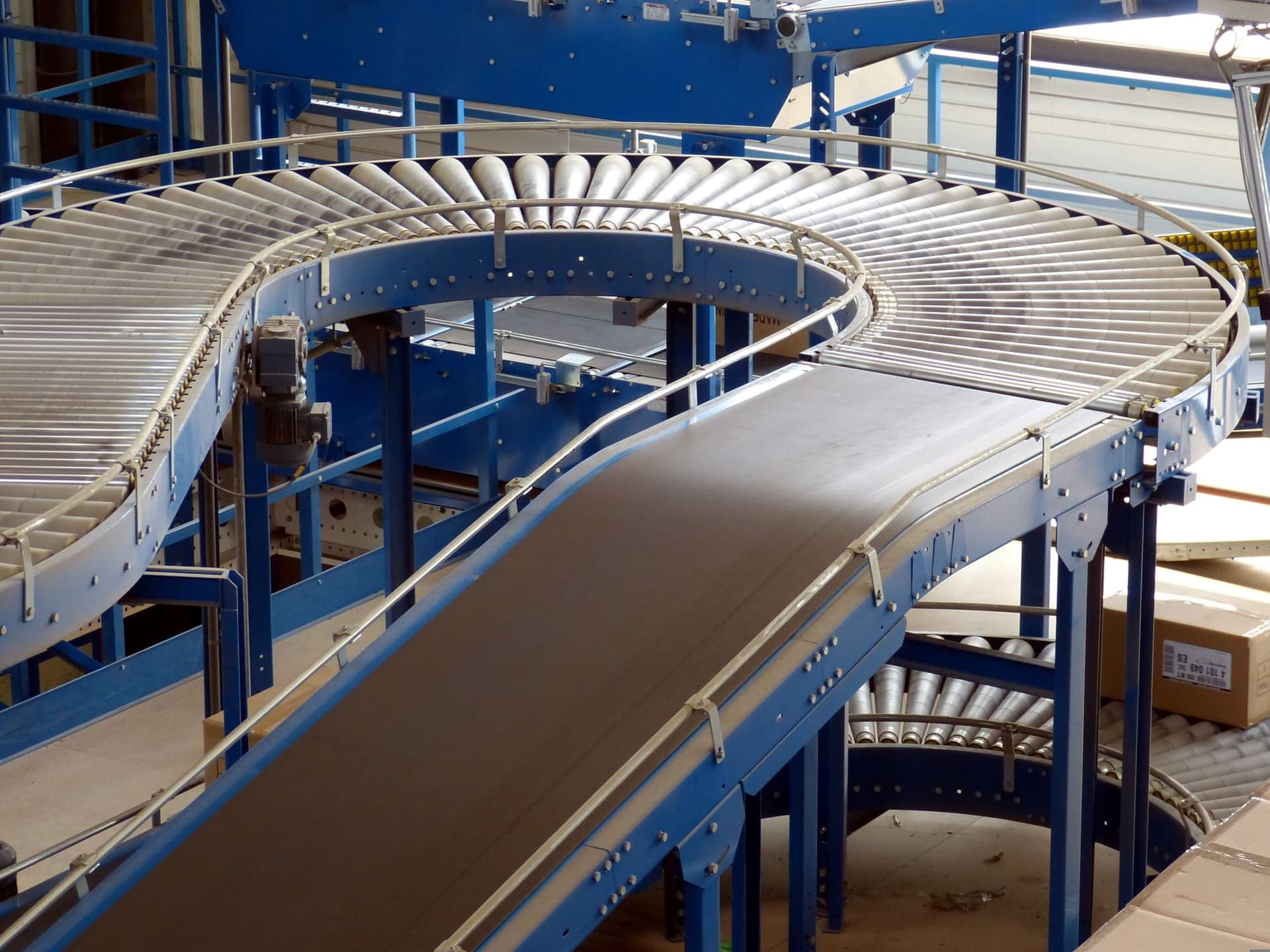 A curved roller conveyor running above a belt conveyor in a factory.